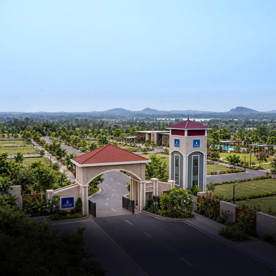 The Pride Green Avenues entrance arch and clock tower, with the tree-lined plotted layout and hills beyond